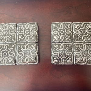 May include: Two sets of four silver-colored ceramic tiles with an intricate Celtic knot design.