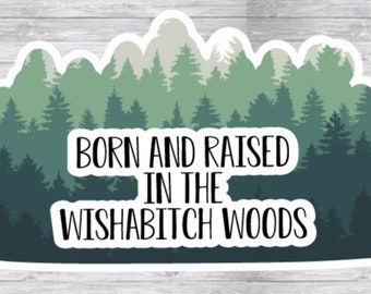 May include: A sticker with a forest scene in shades of green and blue. The text "BORN AND RAISED IN THE WISHABITCH WOODS" is in a bold, white font, overlaying the forest image. The sticker has a white border.