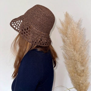 May include: A brown crochet bucket hat with a wide brim and openwork detailing. The hat is made of a textured yarn and has a slightly flared shape. The hat is a stylish accessory for sun protection.