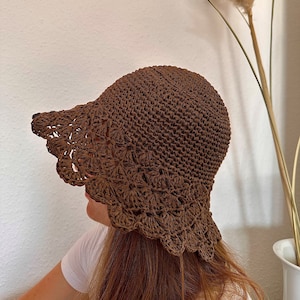 Puede incluir: Un sombrero de sol de crochet marrón con un ala ancha y un borde festoneado.