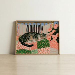 May include: A framed painting of a tabby cat sleeping on a patchwork quilt with green and pink floral patterns. The cat rests against a headboard with vertical black and white stripes, while a cluster of pink flowers sits to the right side.