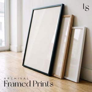 a collection of framed prints arranged on a wooden floor against a white wall.