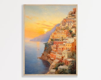 May include: A framed print of a coastal town at sunset. The artwork depicts colorful buildings cascading down a hillside towards the sea. The sky is a blend of orange and yellow hues, with the sun setting over the water. The print is in a light-colored wooden frame.