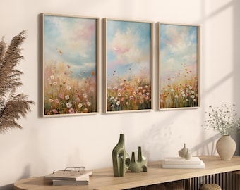May include: Three framed paintings of a field of wildflowers with a light blue sky and fluffy white clouds. The paintings are in a modern style and have a soft, dreamy feel.