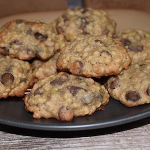 May include: A plate of freshly baked oatmeal chocolate chip cookies. The cookies are golden brown and have a chewy texture. They are arranged in a circle on a black plate with a brown and white striped design.