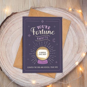 May include: A purple card with the text "You're Fortune Awaits" and a gold crystal ball design. The card is on top of a brown envelope, set on a wooden surface. The text "A Magical Date Night" is visible on the crystal ball.