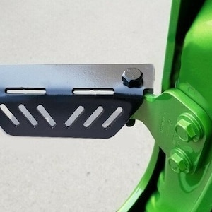 May include: Black metal step with a textured surface and a series of holes. The step is attached to a green door with black bolts.