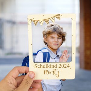 Könnte beinhalten: Ein Holzfotorahmen mit hellbraunem Hintergrund und goldenen Akzenten. Der Rahmen hat einen Ausschnitt für ein Foto und der Text "Schulkind 2024 Moritz" ist unten geschrieben. Ein junger Junge lächelt auf dem Foto.