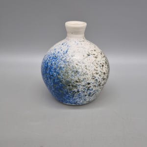 May include: A small, white ceramic vase with a speckled blue and green glaze. The vase has a round body and a narrow neck.