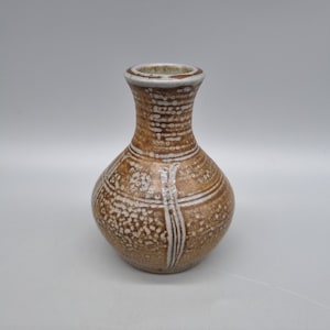 May include: A small, brown ceramic vase with white glaze and a geometric design. The vase has a round body and a narrow neck.