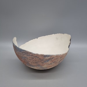 May include: A white ceramic bowl with a textured, uneven rim and a mottled pink and gray glaze.