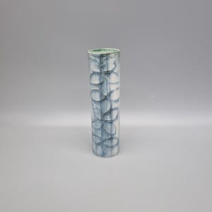 May include: A tall, cylindrical vase with a blue and white floral pattern. The vase has a light green interior and is approximately 25 cm tall. The design features overlapping, stylized leaf shapes. The vase is made of ceramic or a similar material.