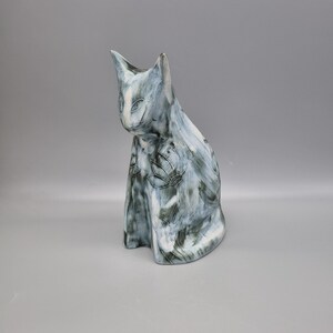 May include: A ceramic cat ornament in blue, grey, and white. The cat is seated with its head tilted. The figurine has a textured finish and floral patterns. The cat's eyes have white detailing. The ornament is suitable for display.