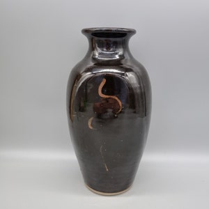 May include: A dark brown ceramic vase with a light brown rim and a simple, abstract design in a lighter brown colour.