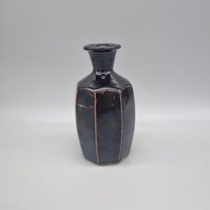 May include: A dark blue ceramic vase with a geometric shape and a narrow neck. The vase has vertical brown lines and a glossy finish. The vase is a decorative item.