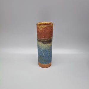 May include: A tall, cylindrical ceramic vase with a textured surface. The top section is reddish-brown, transitioning to a darker band, then a blue and green speckled middle, and a tan base. The vase is approximately 20 cm tall.