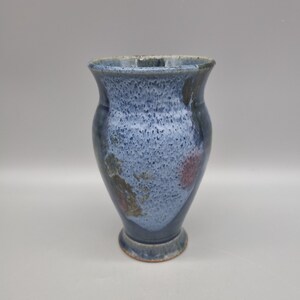May include: A small, blue ceramic vase with a speckled glaze and a slightly flared rim. The vase has a light blue base with a darker blue rim and a speckled glaze.