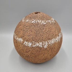 May include: A round, brown ceramic vase with white accents. The vase has a rough, textured surface.
