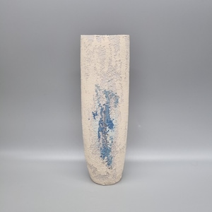 May include: A white ceramic vase with a textured surface and blue paint accents. The vase is tall and slender.