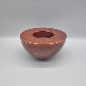 May include: A reddish-brown, semi-spherical decorative bowl with a circular opening in the centre. The bowl has a textured surface and a glossy finish. The interior of the bowl is a darker shade of red-brown.