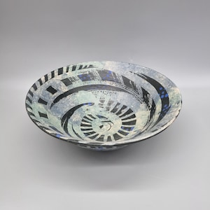 May include: A ceramic bowl with a spiral design. The bowl features a black, white, and blue colour scheme. The interior has a spiral pattern, and the rim has a series of black and white stripes. The bowl is approximately 30 cm in diameter.