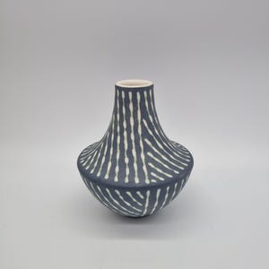 May include: A navy blue ceramic vase with a white interior and a pattern of white, vertical, dashed lines. The vase has a rounded base, a flared body, and a narrow neck. The vase is approximately 8 inches tall.