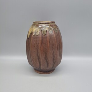 May include: A brown ceramic vase with a textured surface and a light brown glaze. The vase has a rounded shape with a slightly flared opening.