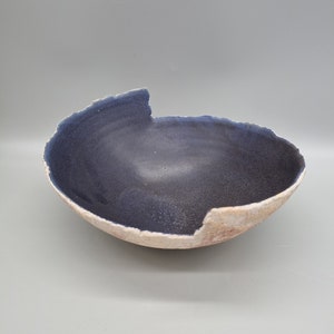 May include: A dark blue ceramic bowl with a white rim and a slightly uneven edge. The bowl is handmade and has a rustic, organic feel.