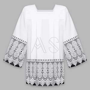 May include: White liturgical alb with lace trim. The lace trim is white and features a floral design. The alb has a square neckline and long sleeves.