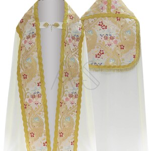 May include: A white liturgical cope with a gold and floral patterned trim. The cope has a matching hood with a gold fringe.