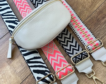Puede incluir: Cinco correas de tela con diferentes patrones para un bolso, todas en blanco, negro y rosa. Las correas están dispuestas sobre una superficie de madera con un bolso de cuero blanco en el centro.