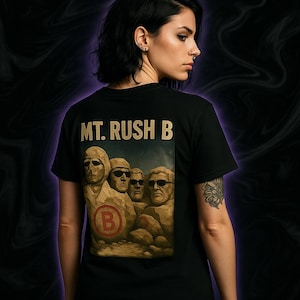 May include: Black t-shirt with a graphic of Mount Rushmore with sunglasses and the text "MT. RUSH B". The graphic includes a red "B" on the mountain. The shirt is made of a soft material.