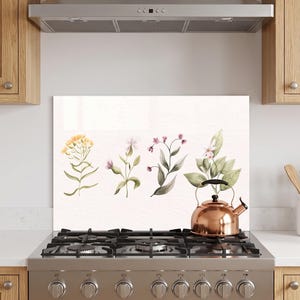 May include: A rectangular kitchen splashback panel featuring a watercolour illustration of four distinct botanical stems with yellow, pink, and green leaves. The panel is positioned behind a stainless steel gas stove with a copper tea kettle.