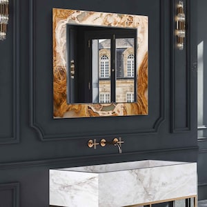 Könnte beinhalten: Ein weißer Marmor-Waschtisch mit einem goldenen Metallrahmen und einem Regal. Der Waschtisch hat ein rechteckiges Waschbecken und zwei goldene Wasserhähne. Der Waschtisch steht vor einer dunkelgrauen Wand mit einem großen, quadratischen, gerahmten Spiegel mit einem braunen und goldenen Marmormuster.