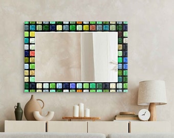 May include: A rectangular mirror with a colorful mosaic frame. The frame is made up of small, square tiles in shades of green, blue, and yellow. The mirror is hanging on a wall in a living room setting.