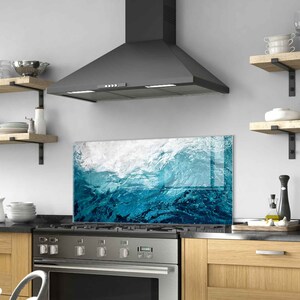 May include: A black range hood with a blue and white wave design glass backsplash. The backsplash is a decorative panel that protects the wall behind the stove from splatters and spills.