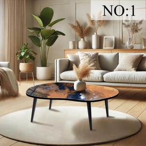 May include: Oval coffee table with an abstract design in orange, blue, and black. The table has a black border and legs. The text "NO:1" is in the upper right corner. The table is set on a white rug. The table's length is approximately 120 cm.