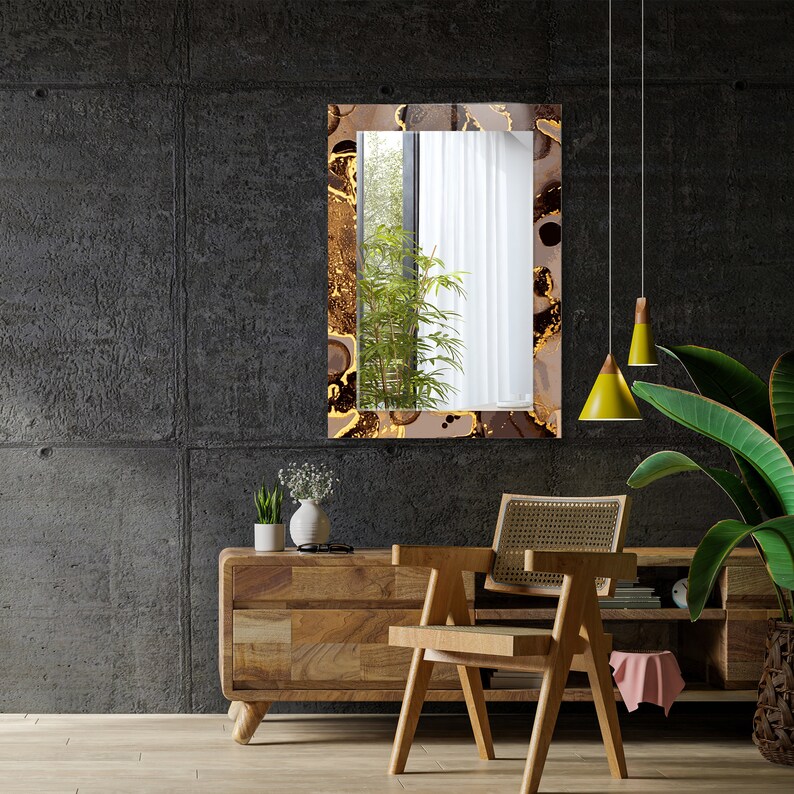 May include: A brown wooden console table with a chair in front of it. The table has two drawers and a shelf. The chair has a woven cane seat and back. A mirror with a gold and brown abstract design hangs on the wall behind the table. Two yellow pendant lights hang from the ceiling.