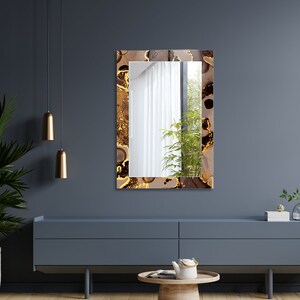 May include: A rectangular mirror with a brown and gold abstract design frame. The mirror is hanging on a dark gray wall above a dark gray dresser.