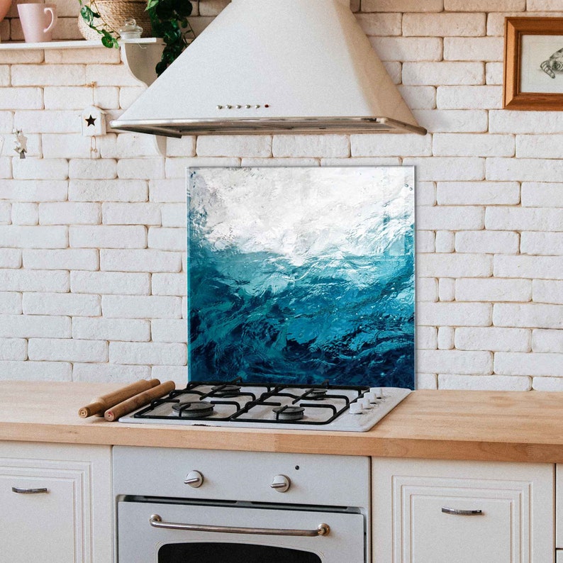 May include: A blue and white abstract ocean wave design kitchen backsplash. The backsplash is installed behind a white gas stove with four burners.