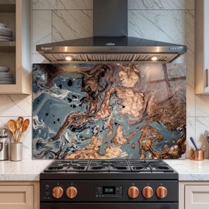 May include: A decorative kitchen backsplash with a swirling abstract design in shades of gray, black, and copper. The backsplash is installed behind a black gas range with copper-colored knobs and a stainless steel range hood.