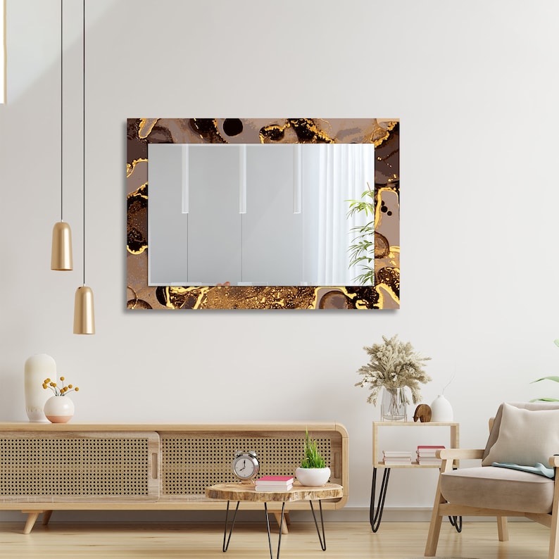May include: A rectangular mirror with a brown and gold abstract design frame. The mirror is hanging on a white wall above a wooden cabinet.