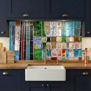 May include: A colorful stained glass backsplash with a variety of rectangular and square glass pieces in shades of blue, green, red, and yellow. The backsplash is installed above a white farmhouse sink and wooden countertop in a kitchen.