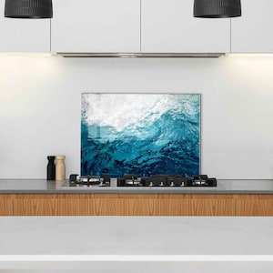 May include: A blue and white abstract wave design glass kitchen backsplash. The backsplash is installed above a gas stovetop.
