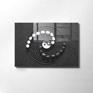 May include: A black and white yin yang symbol surrounded by white stones in a spiral pattern on a black sand zen garden.