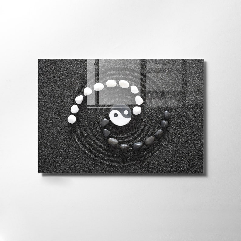 May include: A black and white yin yang symbol surrounded by white stones in a spiral pattern on a black sand zen garden.