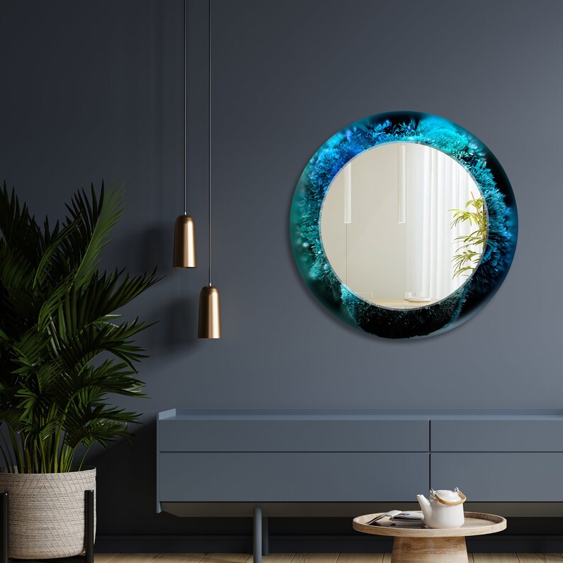 Pu&ograve; includere: Uno specchio rotondo con un design astratto blu e verde che circonda la superficie riflettente. Lo specchio &egrave; appeso a una parete blu scuro.