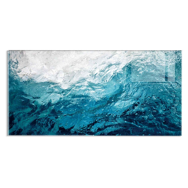 May include: A close-up of a blue ocean wave with white foam breaking on the surface. The water is clear and you can see the ripples and bubbles.