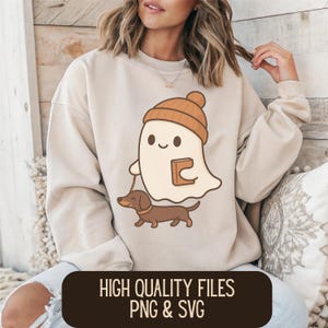 Puede incluir: Sudadera beige con un fantasma de dibujos animados con gorro marrón y un libro, paseando a un perro salchicha marrón. El texto "HIGH QUALITY FILES PNG & SVG" está en un rectángulo marrón en la parte inferior.