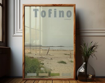 May include: A framed print featuring a beach scene with the word "Tofino" and "CANADA" in light gray text. The frame is made of wood, and the image shows a sandy beach, ocean, and sky. A clear glass vase with green plants sits on a wooden floor.